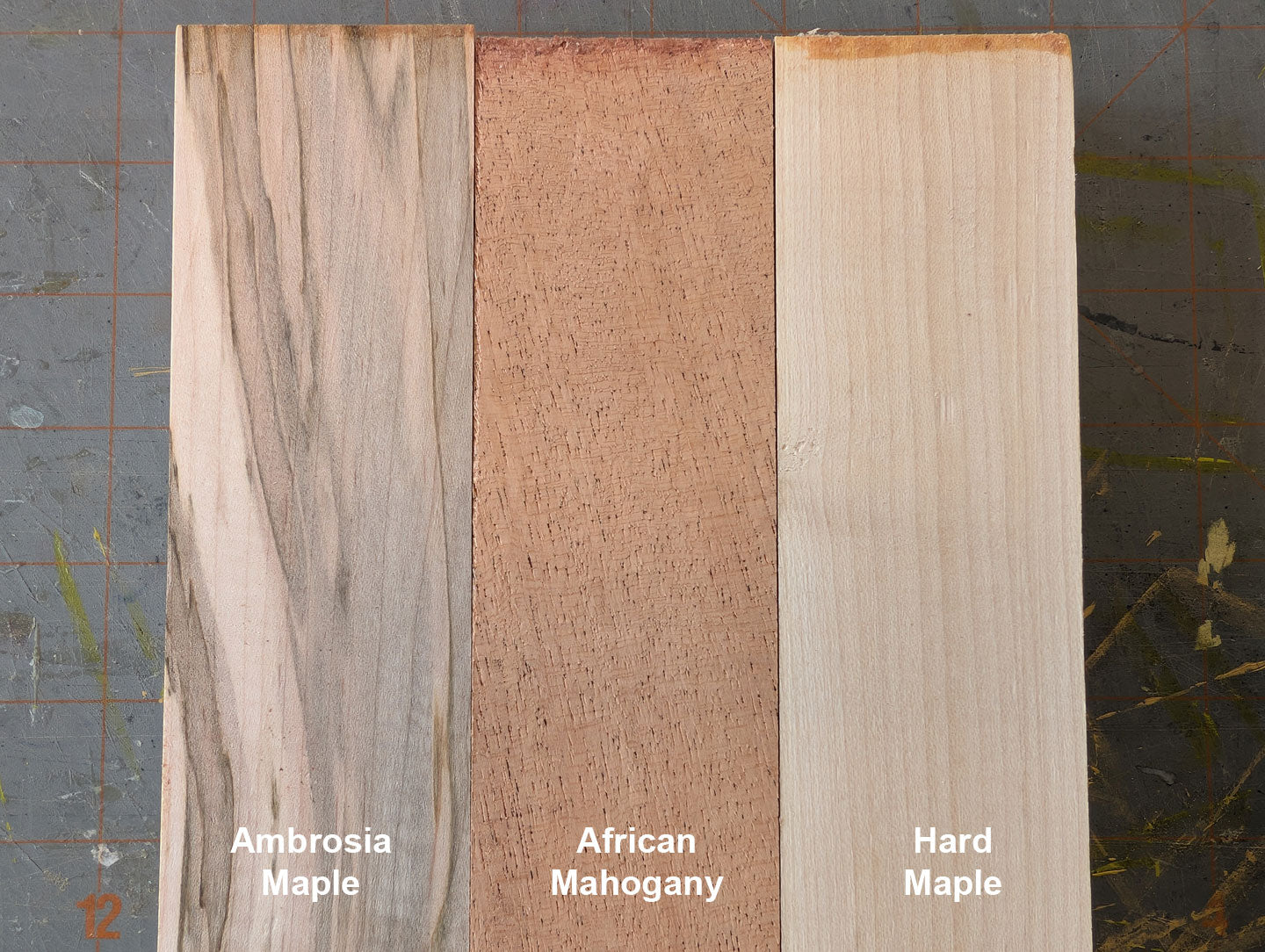 Three types of wood samples labeled 'Ambrosia Maple', 'African Mahogany', and 'Hard Maple' on a textured background.