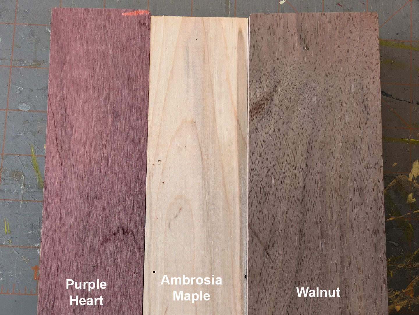 Three wooden planks labeled 'Purple Heart', 'Ambrosia Maple', and 'Walnut' on a textured background.